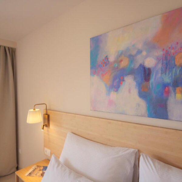 An old painting with vibrant colours placed above white pillowed bed