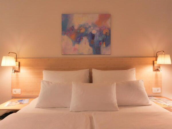 Double bed with neatly arranged pillows, night lamps and painting above