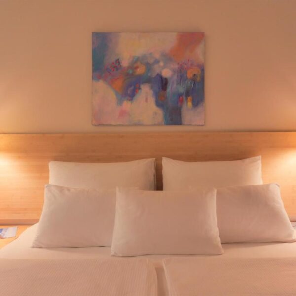 Double bed with neatly arranged pillows, night lamps and painting above