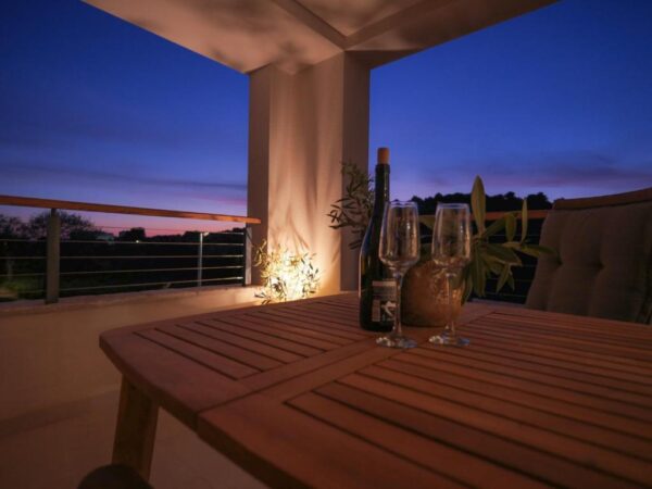 View of the lit up balcony in the evening with wine and glasses on the lounge table