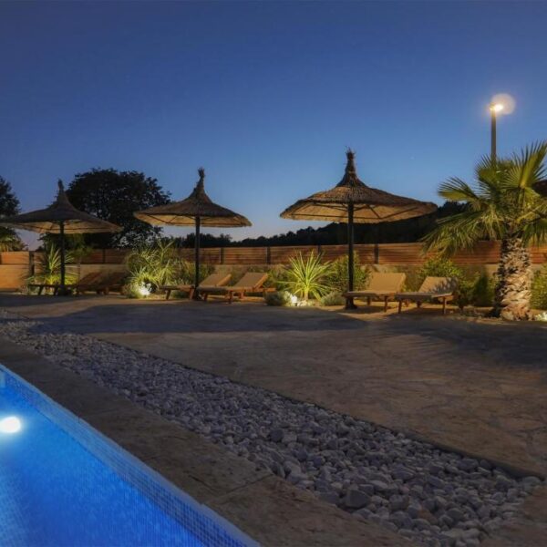 Evening view of illuminated outside pool and terrace with sun loungers and palms