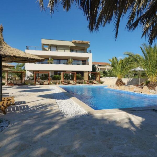 View of the villa from the courtyard with big outside pool and terrace with sunloungers covered with sunlight