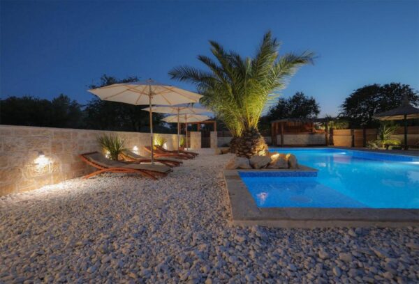 Nightview of illuminated pool surrounded with sun loungers on a white rock covered terrace