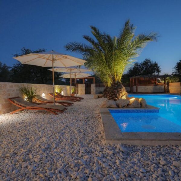 Nightview of illuminated pool surrounded with sun loungers on a white rock covered terrace
