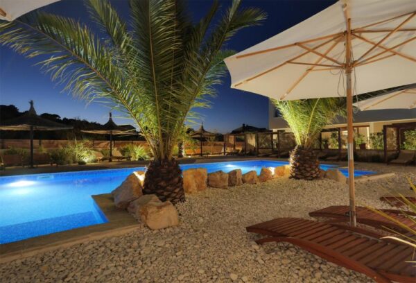 Evening view of illuminated outside pool and terrace with sun loungers and palms